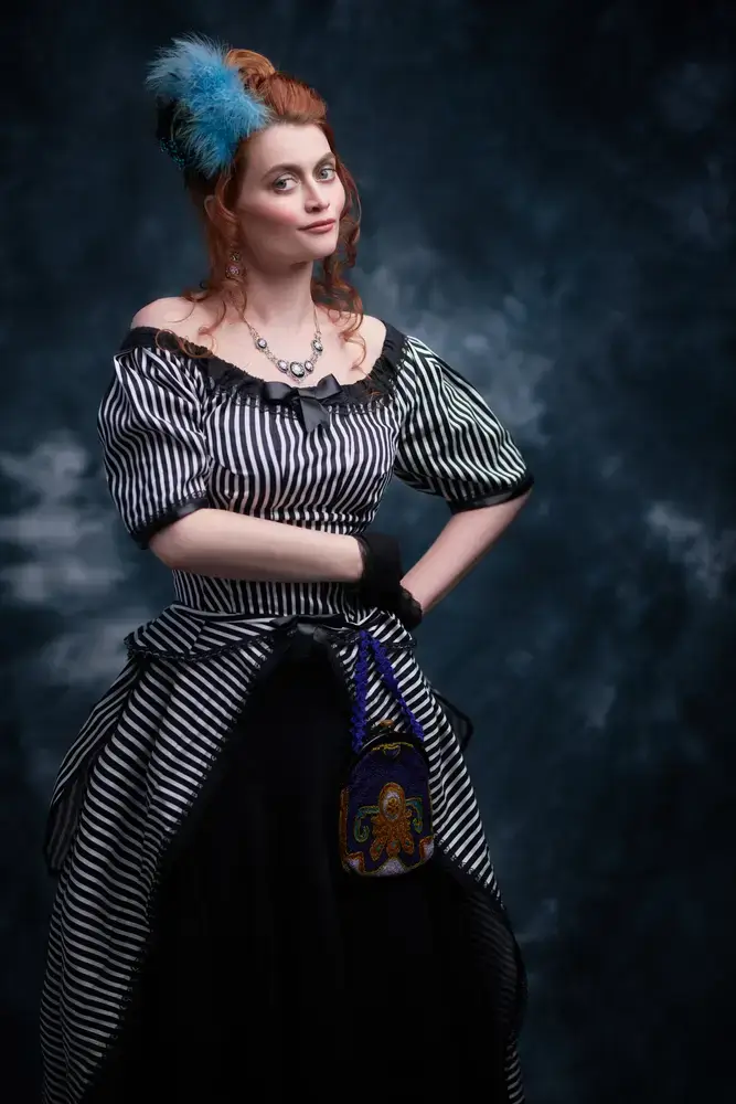 Femme à la mode du 19eme siècle en robe à rayures verticales noires et blanches Elle tient un sac à main d'époque dans sa main au niveau des hanches