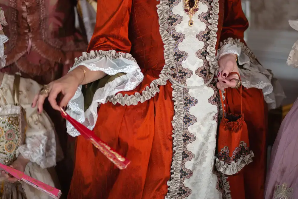 Femme en robe rouge du style renaissnce qui tient un éventail dans sa main droite et un sac à main dans sa main gauche