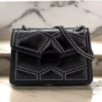 Sac à main noir matelassé avec chaîne cloutée fermé, vu de face posé sur un fond en marbre.