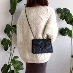 Sac à main noir matelassé avec chaîne cloutée porté à l'épaule dans le de dos de façon bandoulière. on distingue la longueur de la chaine du sac à main qui permet de le porter assez bas .