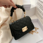 : Mini sac à main noir à bandoulière chaînette dorée présenté avec un décor de boites blanches