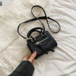 Mini sac à main noir design et élégant sur un canapé avec un fond blanc