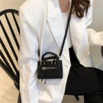 Mini sac à main noir design et élégant en bandoulière porté sur le coté drit par une femme