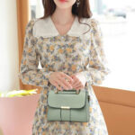 Mini sac à main vert élégant à bandoulière, porté dans la main d'une femme dans une robe motif floral.