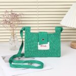 Mini sac à main vert style pochette effet tricoté devant un store crème