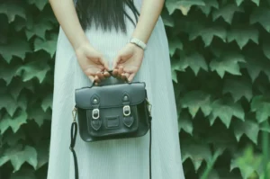 Femme devant un mur de ierre sui tien un sac à main oir dans son dos