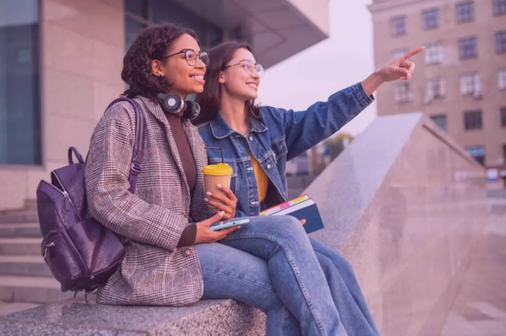 Deux jeunes femmes assises sur les marches de la fac avec un sac à dos en guise de sac à main pour les cours