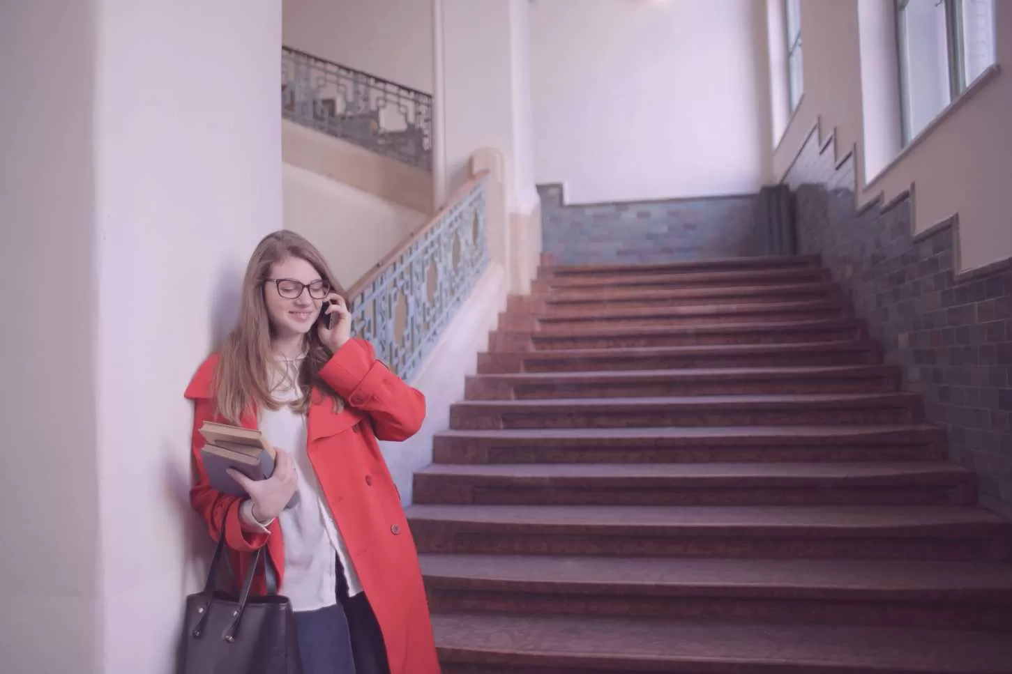 Jeune femme aau téléphone avec un sac à main et des livres de cours dans les mains dans l'escaliers de l'université