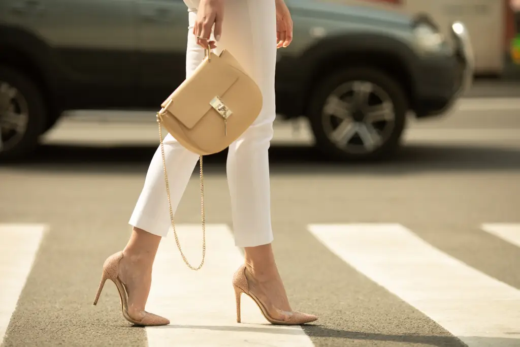 Femme dans la rue qui tient négligemment un sac à main beige