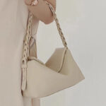 Sac à main beige élégant et design en cuir, porté par une femme.