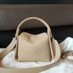 Sac à main beige en simili cuir avec bandoulière large posé sur un tissus blanc