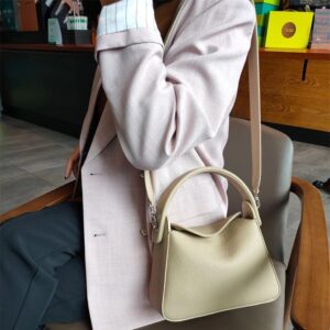 Sac à main beige en simili cuir avec bandoulière large, porté par une femme assise