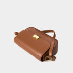 Sac à main camel chic en cuir souple posé sur un support blanc