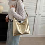 Sac à main doré luxueux et minimaliste porté à l'épaule par uen jeune femme
