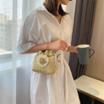 Sac à main été beige à bandoulière avec fleur porté par une femme en robe blanche