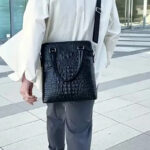 Sac à main homme cuir noir élégant et sophistiqué porté à l'épaule par un homme en chemise blanche