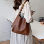 Sac à main marron à bandoulière réglable en simili cuir, porté à l'épaule