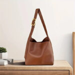 Sac à main marron à bandoulière réglable en simili cuir, posé sur une table en bois.