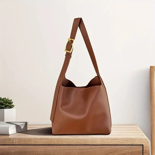 Sac à main marron à bandoulière réglable en simili cuir, posé sur une table en bois.
