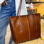 sac à main marron en cuir grand format tenu ar une femme