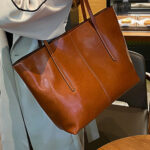 Sac à main marron en cuir grand format, sur un fond blanc porté à l'épaule