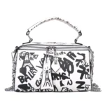 Sac à main original blanc avec des graffitis noirs, incluant des dessins de la Tour Eiffel. Le sac possède une poignée et des détails métalliques.