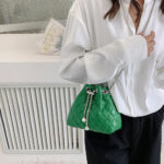 Sac à main vert élégant matelassé en similicuir, porté par une femme en chemise blanche.