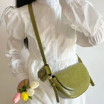 Sac à main vert en similicuir petit format à bandoulière, porté par une femme dans une tenue blanche.
