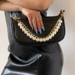 Sangle de sac à main dorée élégant à maillons et perles, sur un sac à main noir et tenu à la main