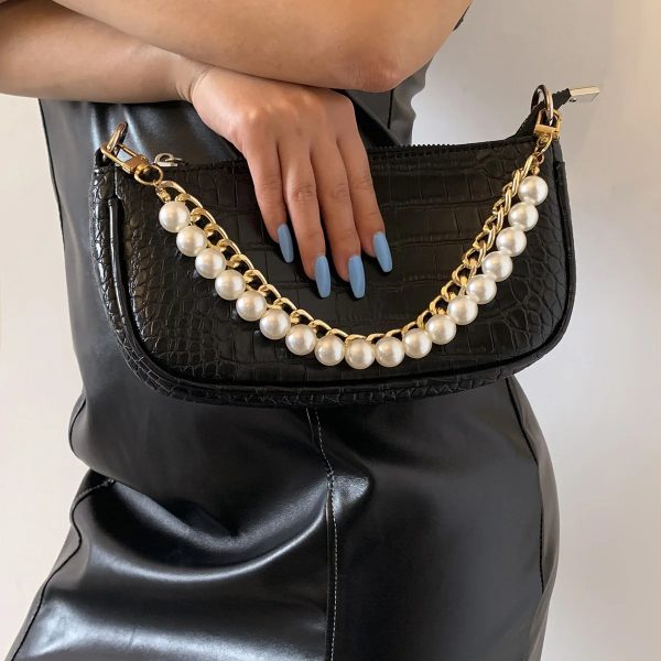 Sangle de sac à main dorée élégant à maillons et perles, sur un sac à main noir et tenu à la main